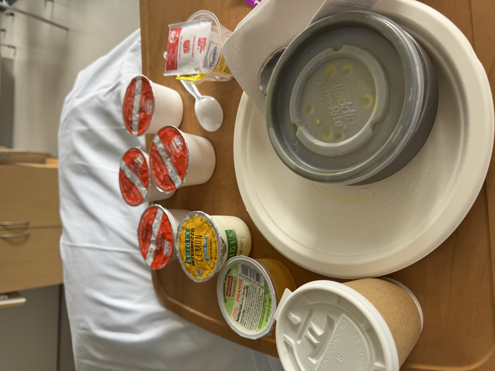 A hospital food tray with juice cups, yogurt, coffee, and condiments