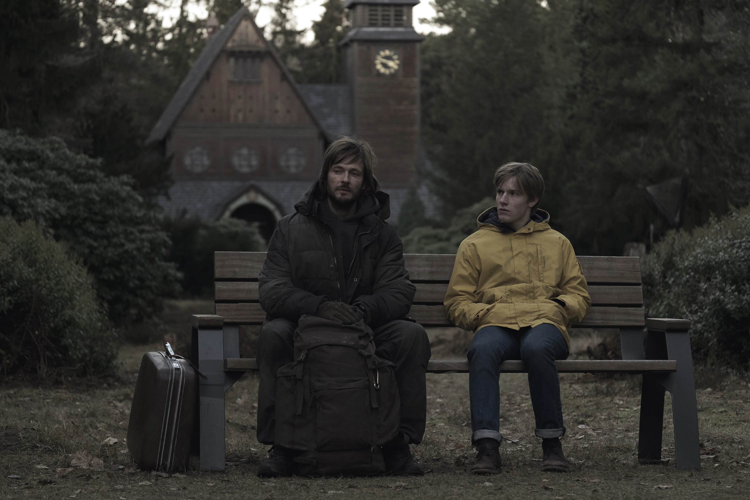 The Stranger and young Jonas sitting on a bench in front of a church, from Dark